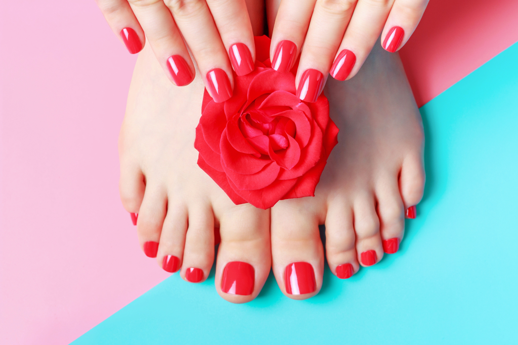 Female hands with manicure and feet with pedicure on blue and pink background.