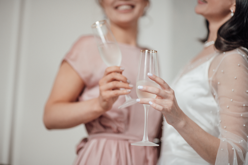 Two millennial candid lifestyle brunette girls in bridal outfits are having fun drinking champagne.