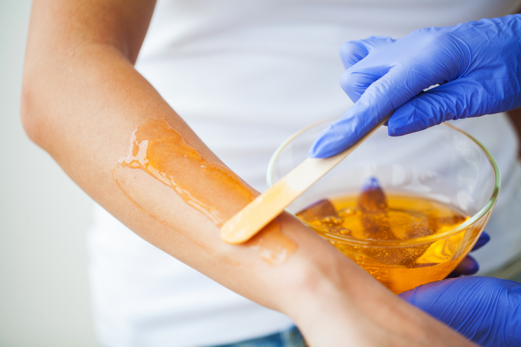 Women hold orange paraffin wax bowl. Woman in beauty salon